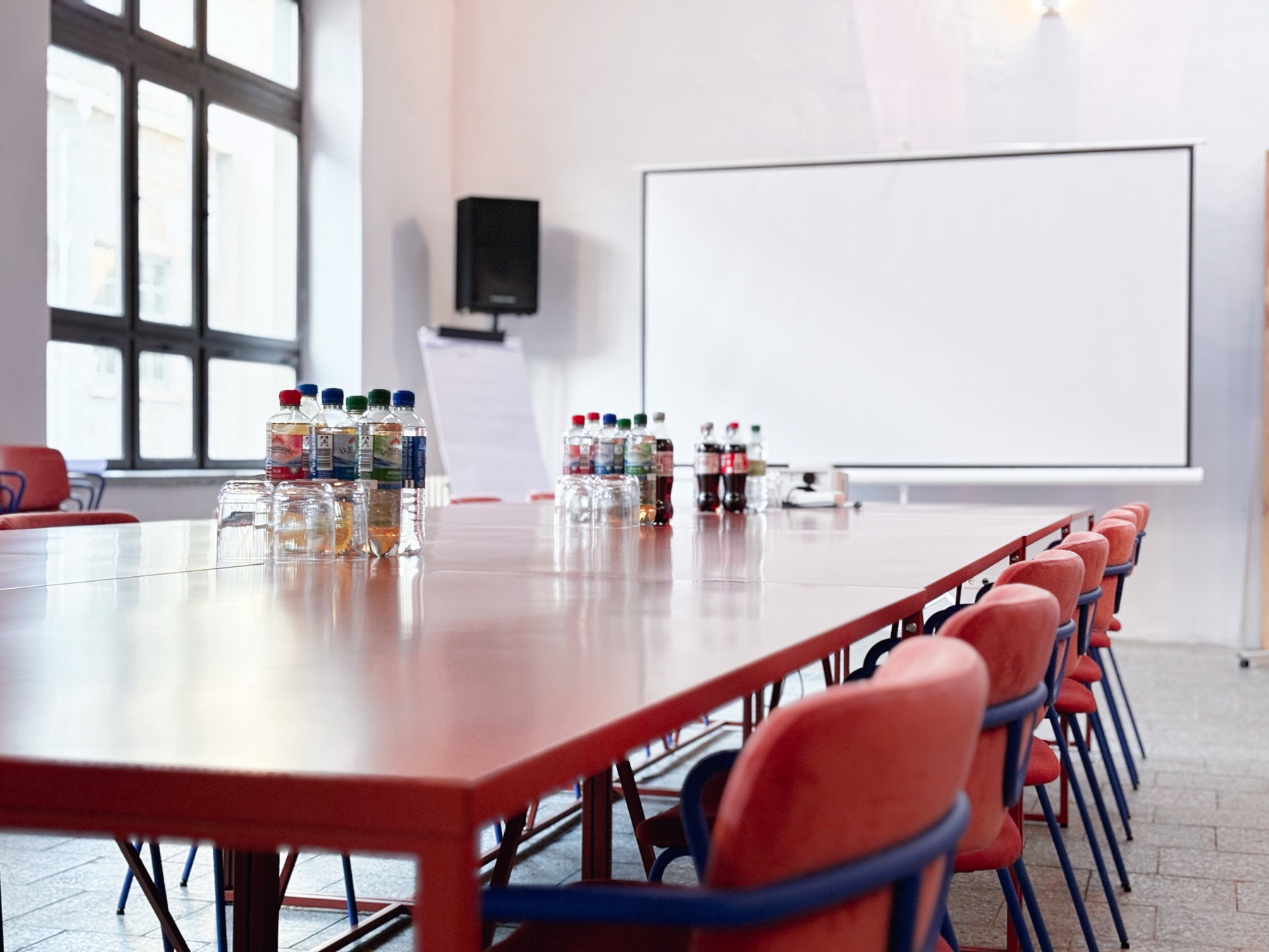 Seminarraum im Obergeschoss mit langer Tafel, roten Stühlen, Getränken und Whiteboard